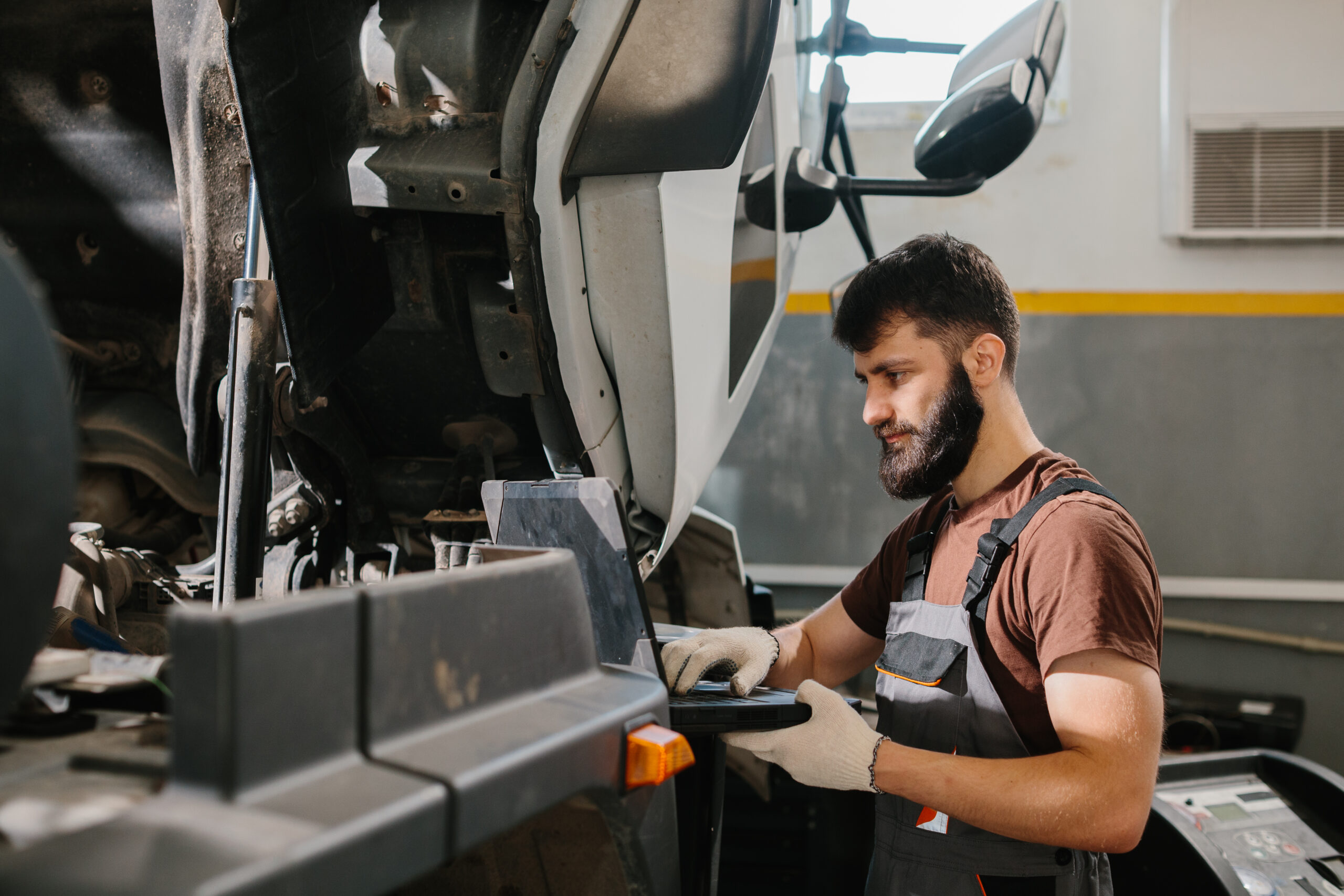 Mechanic using laptop while repairing truck in garage